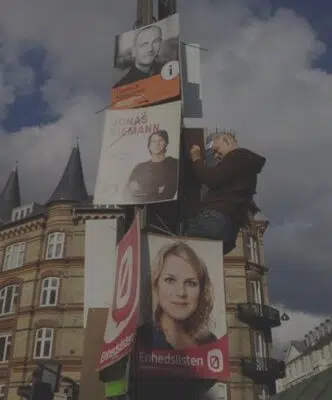 Person monterer valgplakater på en lygtepæl i bymiljø under kommunalvalget
